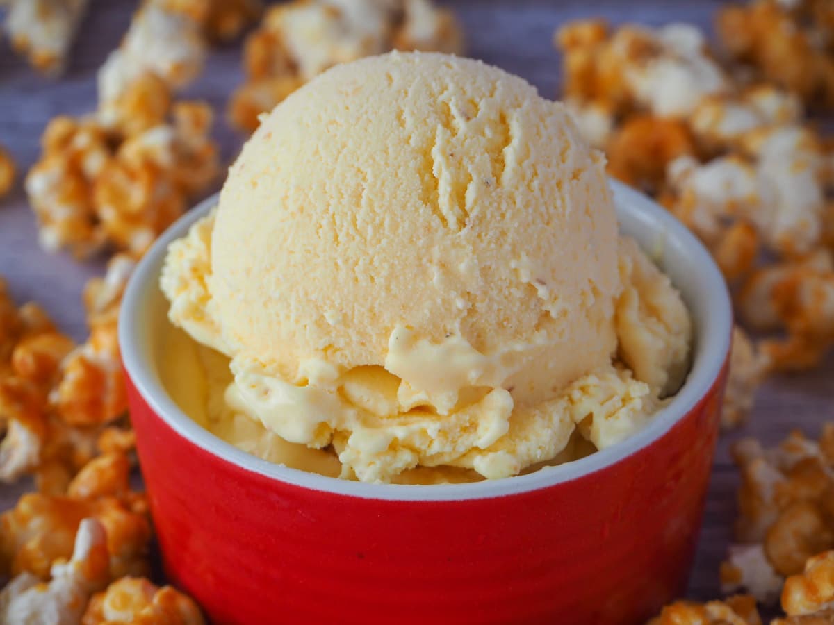 Popcorn ice cream in a red bowl, surrounded by caramel popcorn.
