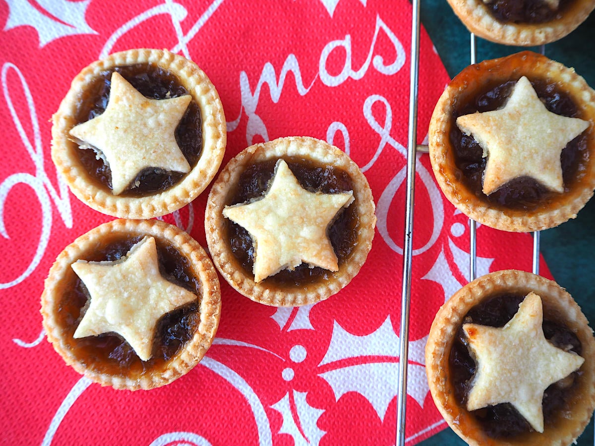 Mincemeat tarts on a Christmas serviette, next to mincemeat tarts on a cooling rack.