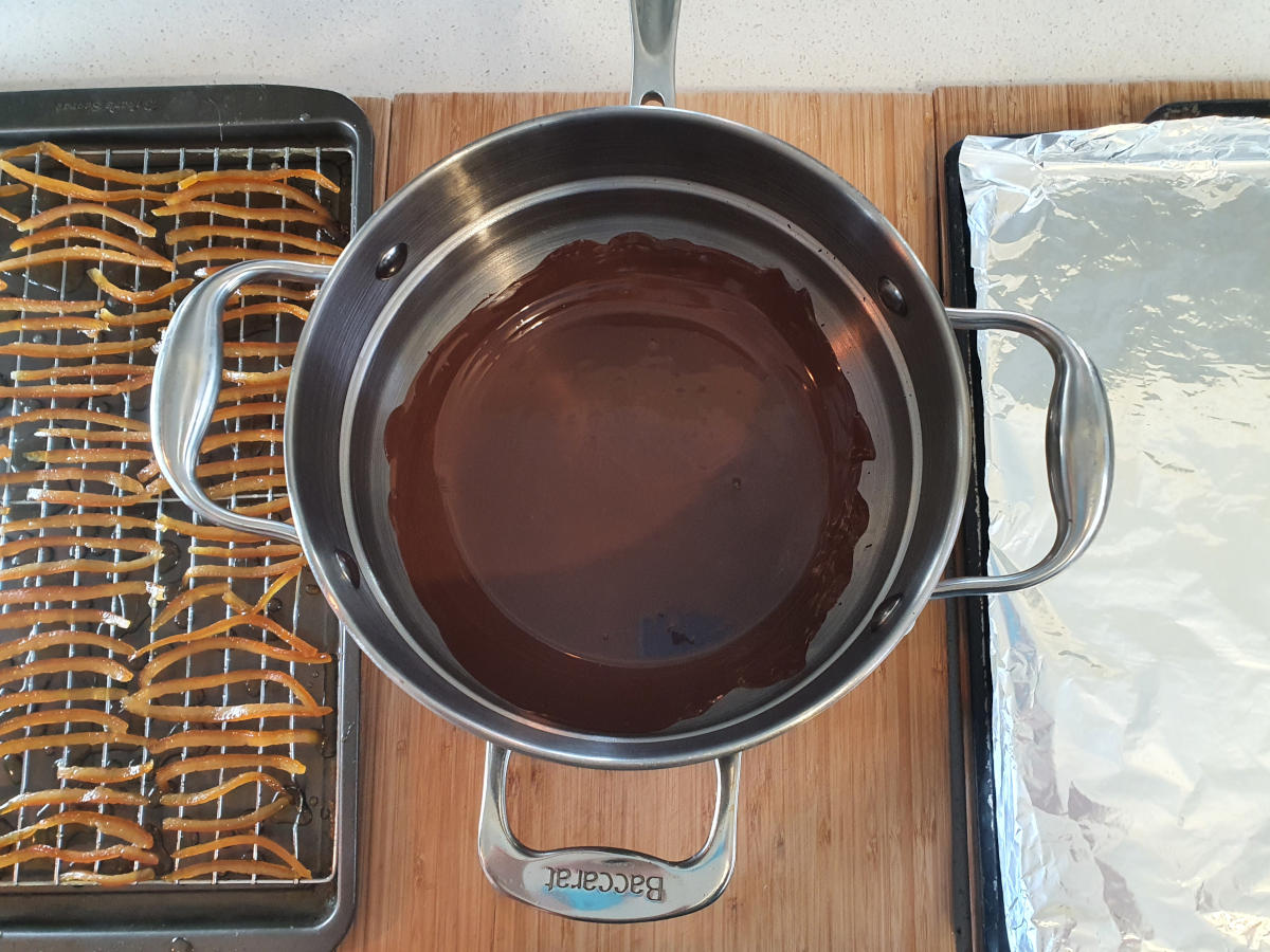 setting up for chocolate covering, tray of dried peel on the left, double boiler with melted chocolate in the middle, tray covered in foil on the right.