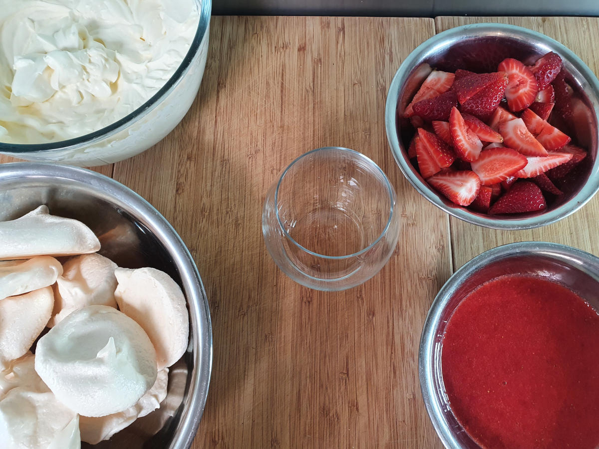 made up ingredients ready to assemble, cream mix, meringues, chopped strawberries and strawberry sauce.