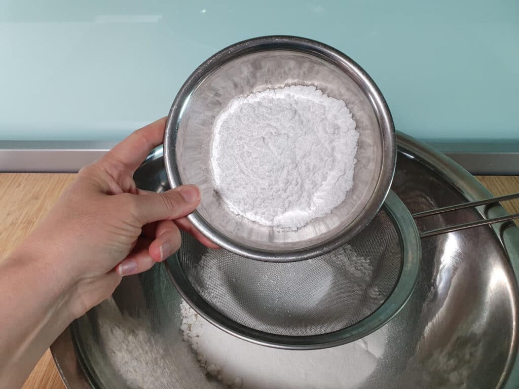 Gluten free shortbread 7 sifting icing sugar into mix in bowl.
