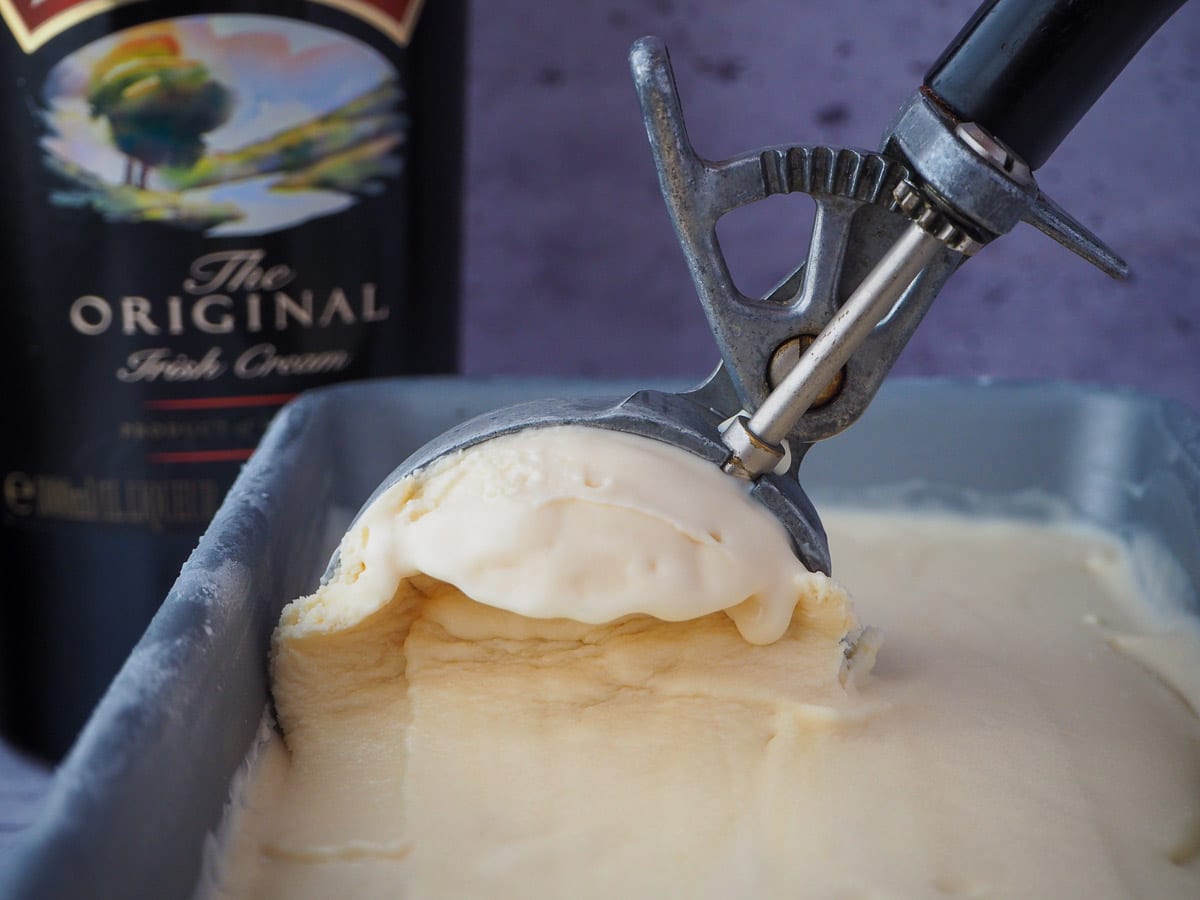 Scooping Baileys ice cream from a pan with a black vintage ice cream scoop and bottle of Baileys in the background.