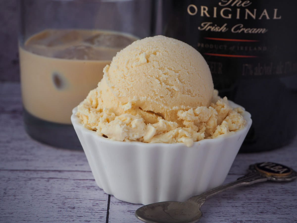 Baileys ice cream scoop with a vintage spoon on the side and glass of Baileys and bottle of Baileys in the background.