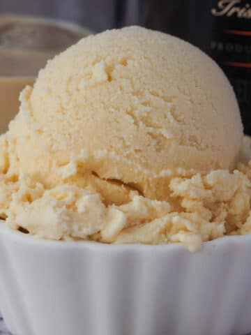 Close up Baileys ice cream scoop with glass of Baileys and bottle of Baileys in the background.