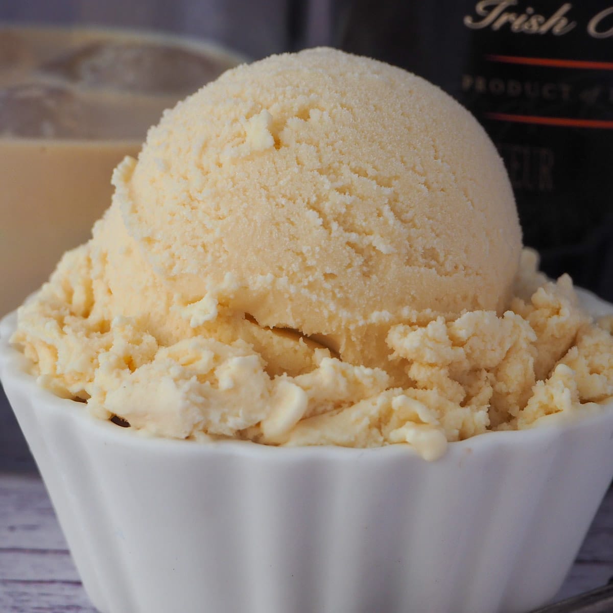 Close up Baileys ice cream scoop with glass of Baileys and bottle of Baileys in the background.