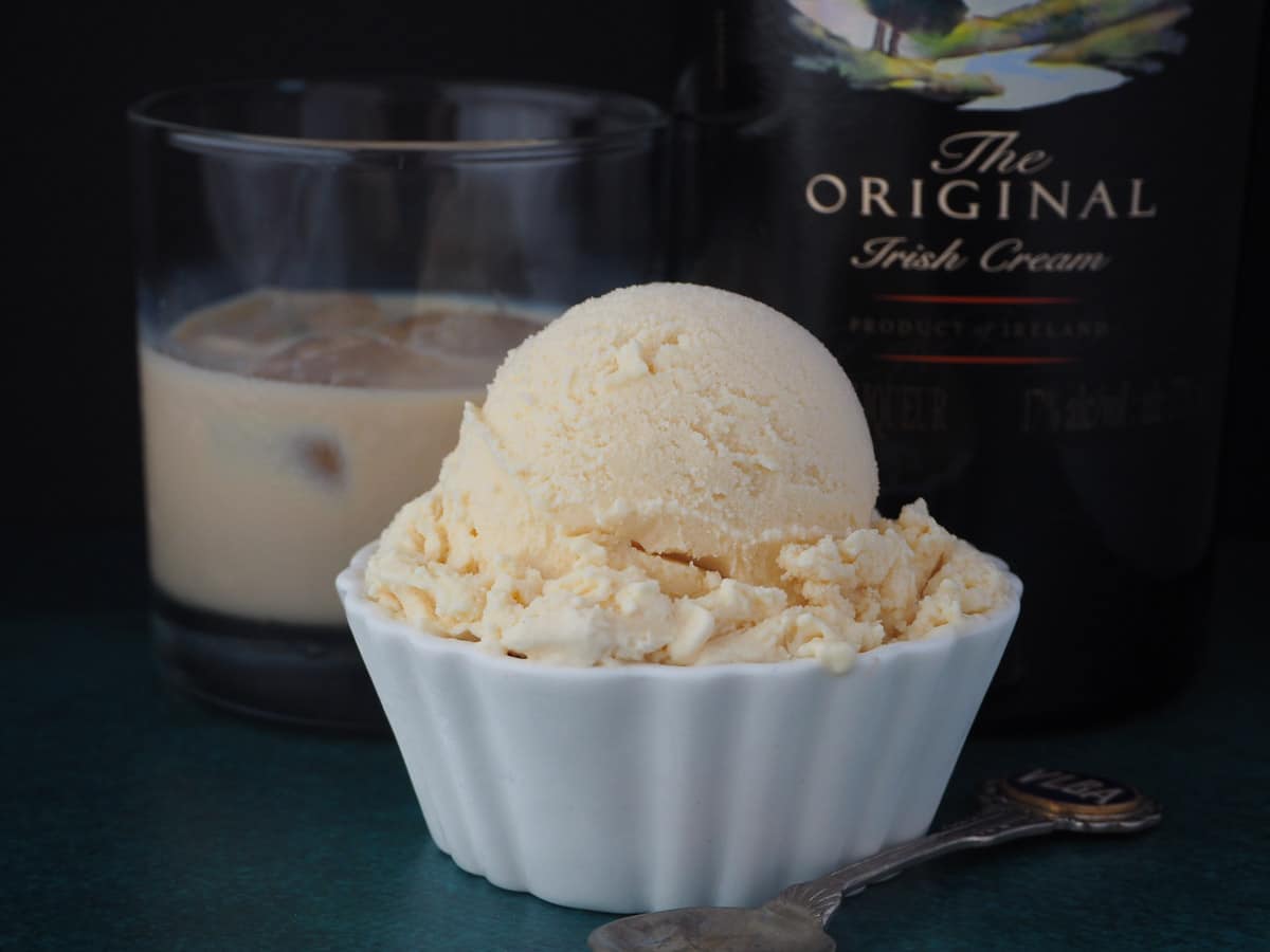 Baileys ice cream scoop with a vintage spoon on the side and glass of Baileys and bottle of Baileys in the background.