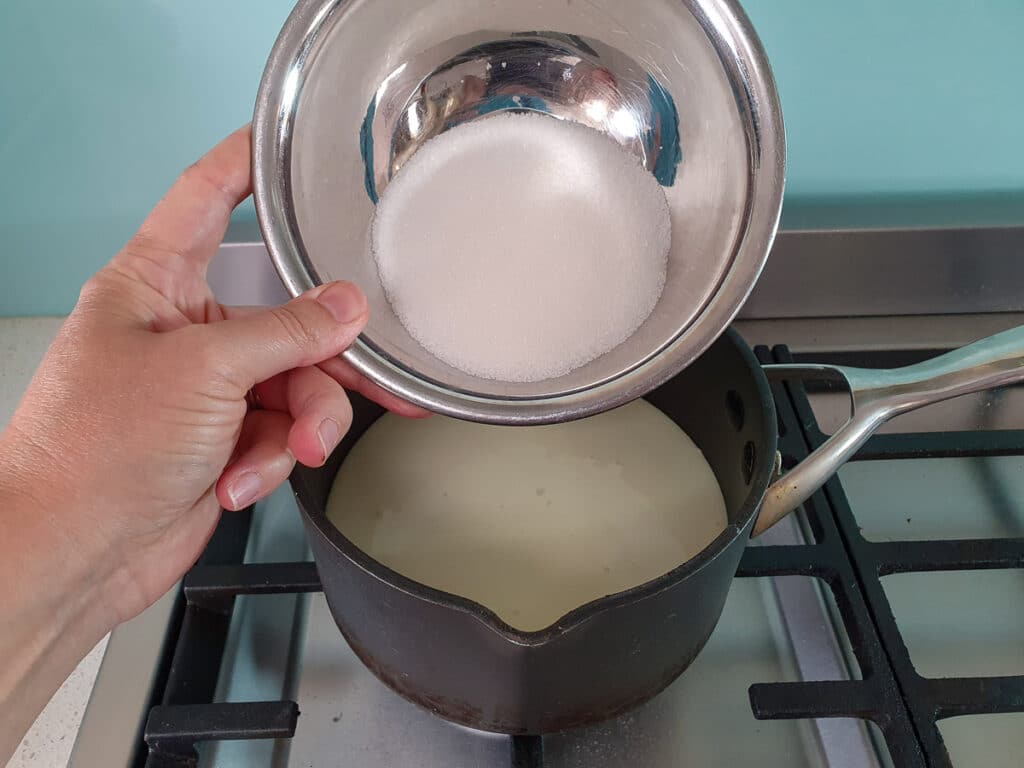 Adding sugar to pot on stove.