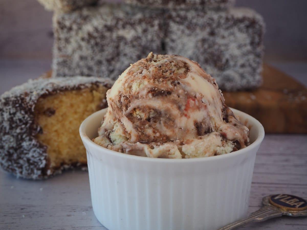 Scoop of lamington ice cream with vintage spoon on the side, in front of stacked lamingtons on a board,