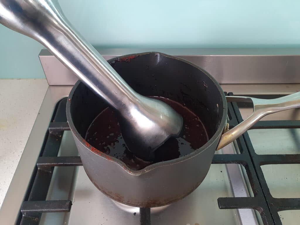 Blitzing chocolate sauce with a stick blender to smooth out lumps.