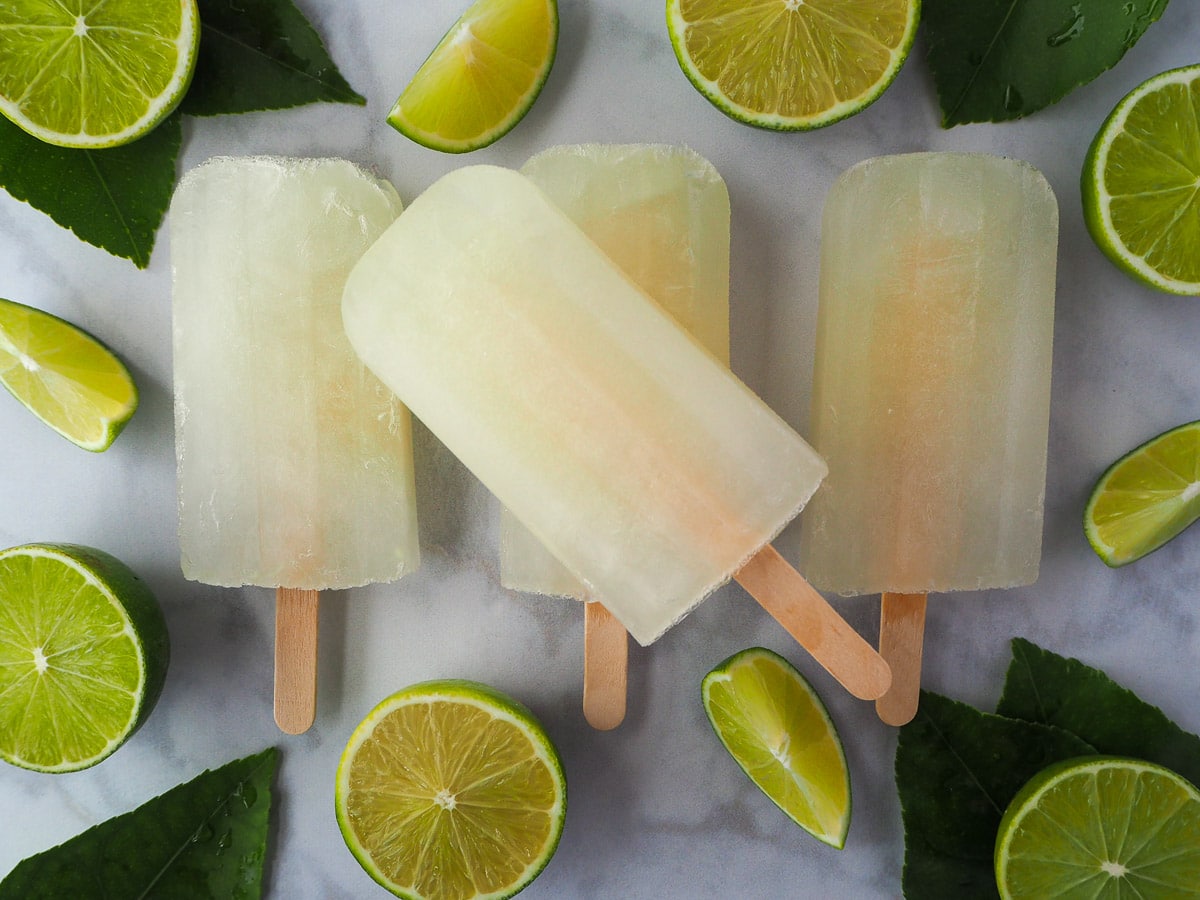 Row of three lime popsicles, with a single lime popsicle on top, surrounded by fresh cut limes and leaves.