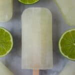Lime popsicles surrounded by fresh cut limes.
