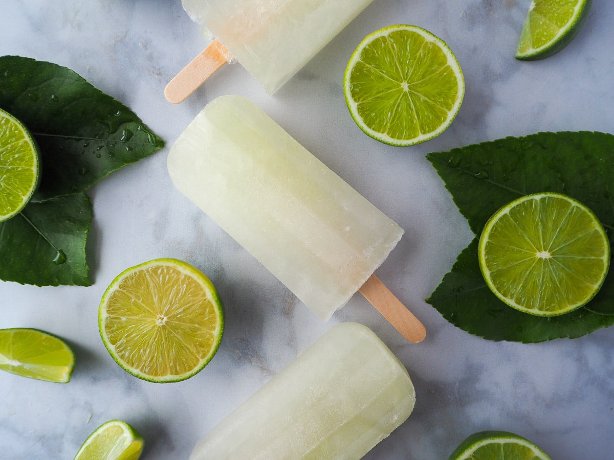 Lime popsicles surrounded by fresh cut limes on a marble background.