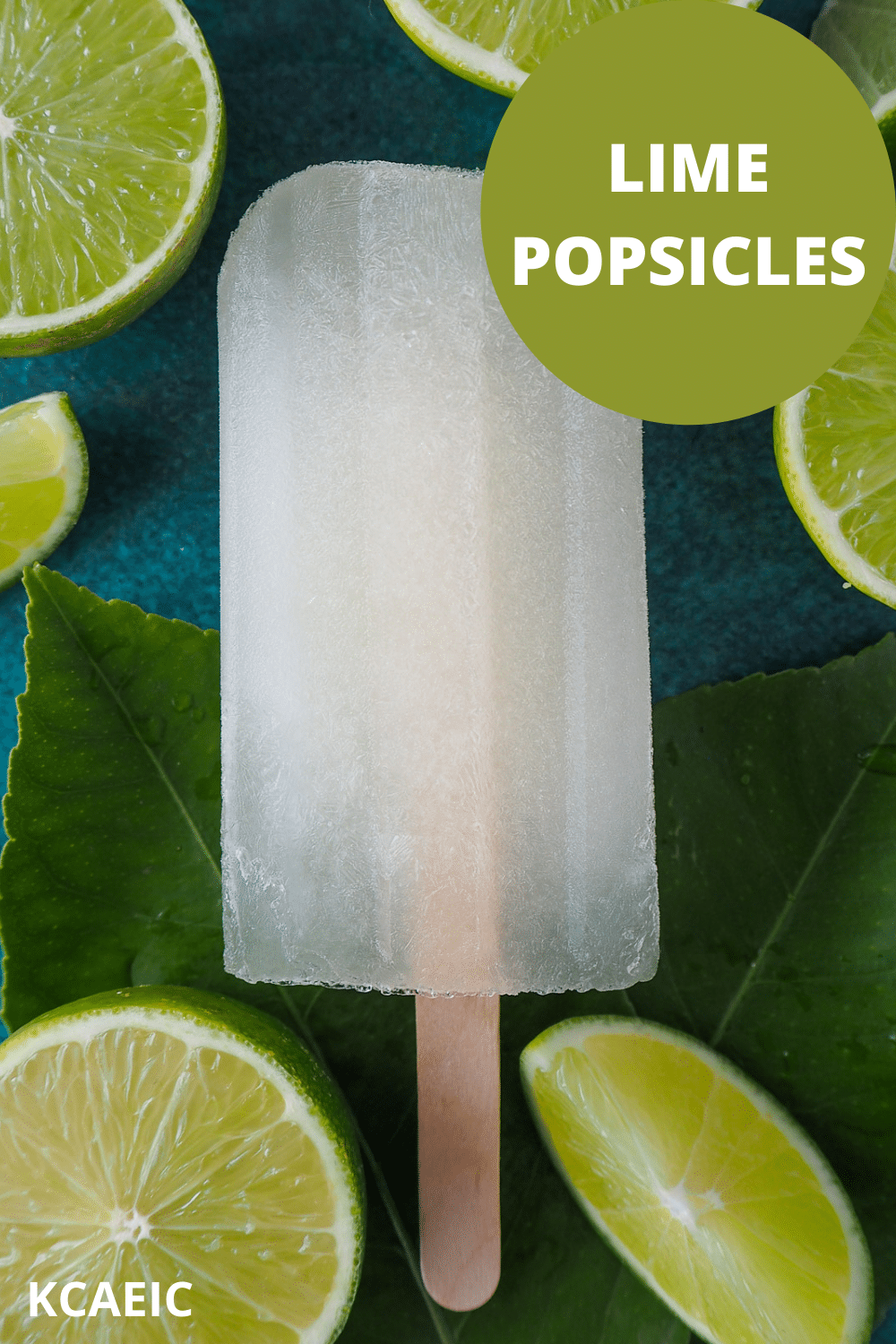 Single lime popsicle on leaves, surrounded by fresh cut up limes, with text overlay, lime popsicles, KCAEIC.