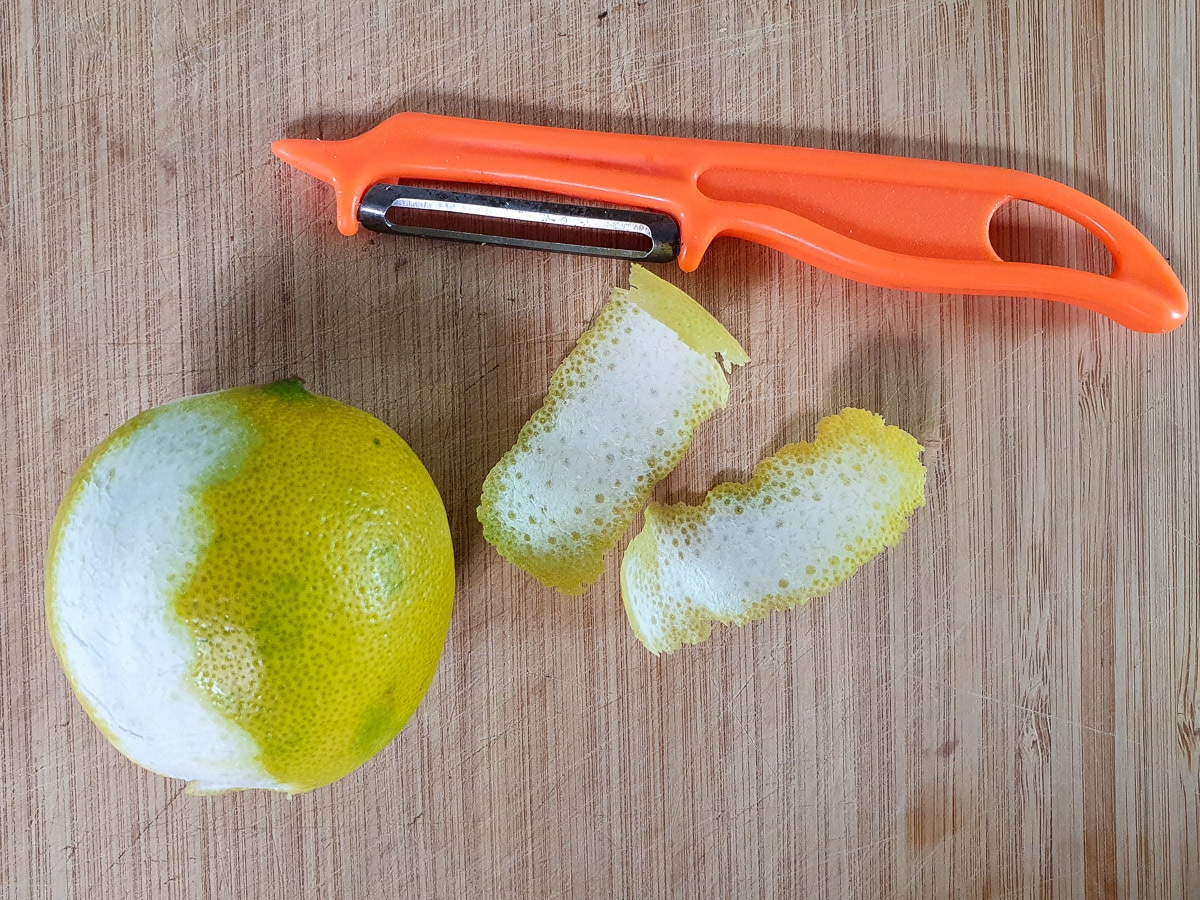 Using a peeler to peel zest strips off two limes.