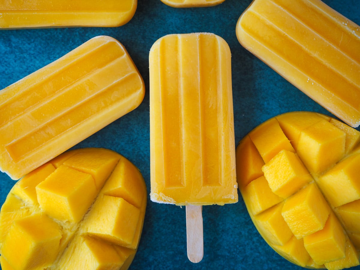 Mango popsicles 11 Mango popsicles surrounded by fresh mango pieces.