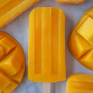 Close up of single mango popsicle, surrounded by fresh mango.