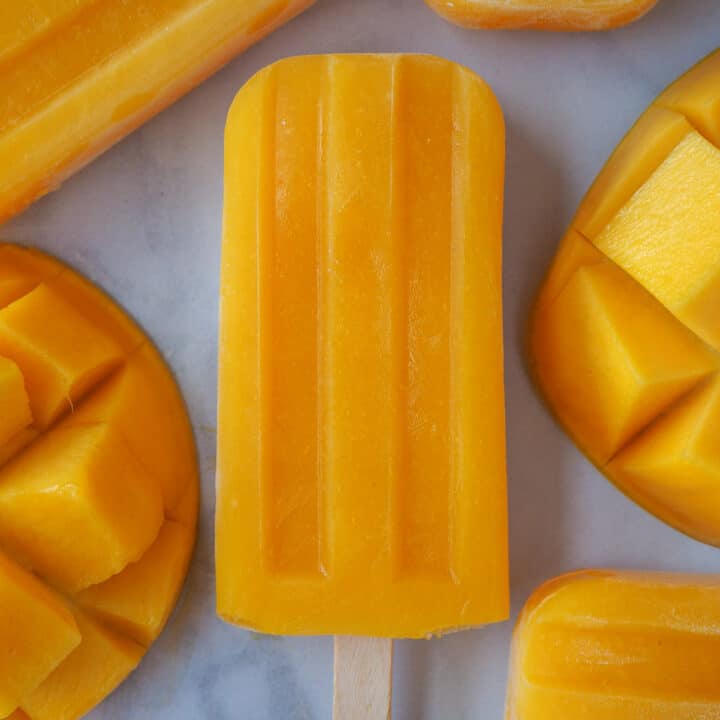 Close up of single mango popsicle, surrounded by fresh mango.