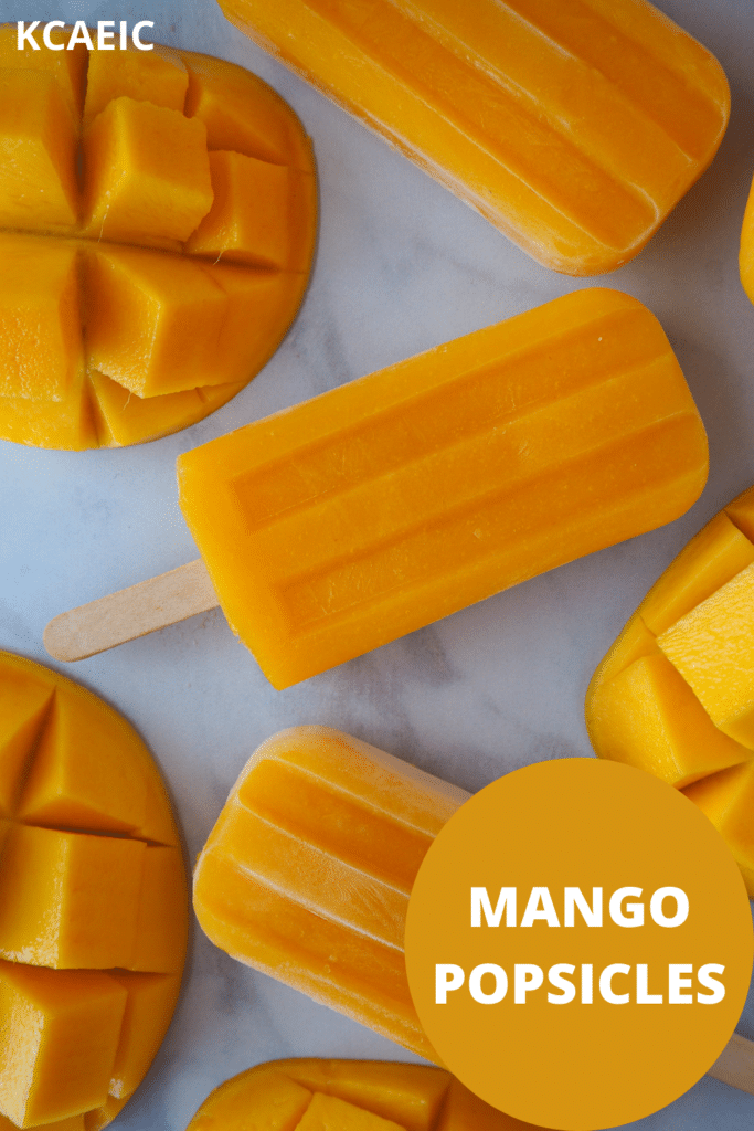 Row of three mango popsicles in a vertical row, surrounded by fresh mango, with text overlay, KCAEIC and mango popsicles.