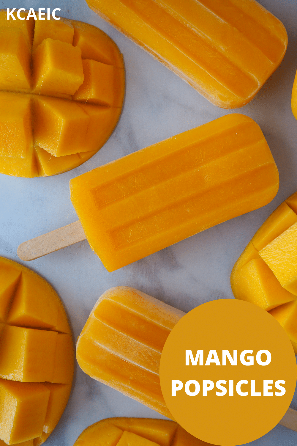 Row of three mango popsicles in a vertical row, surrounded by fresh mango, with text overlay, KCAEIC and mango popsicles.