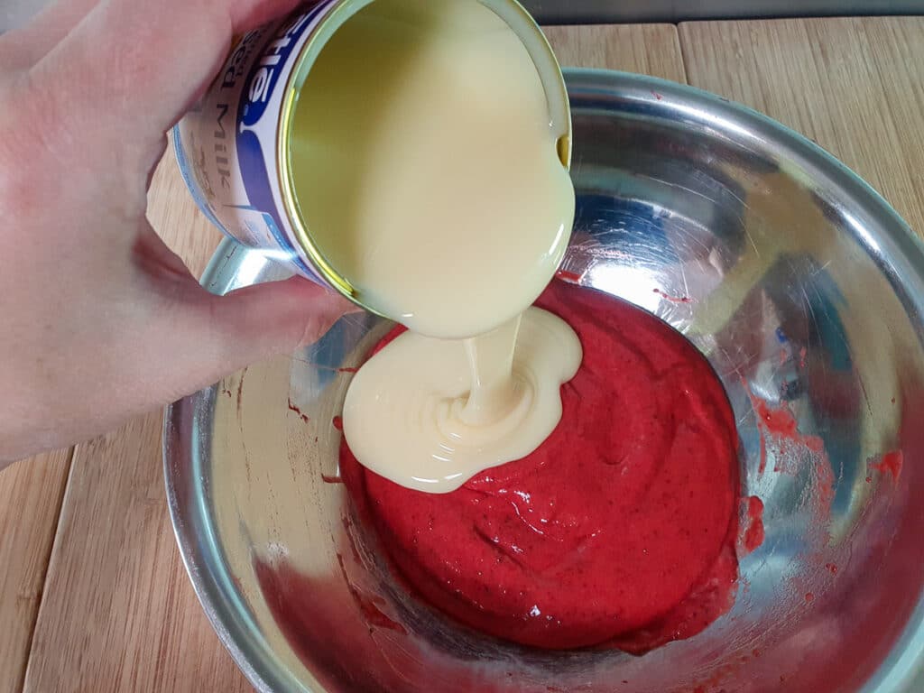Adding tin of sweetened condensed milk to strawberry pulp.