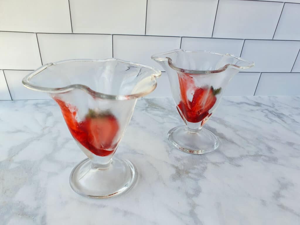 Adding fresh strawberries to the bottom of the sundae glass.