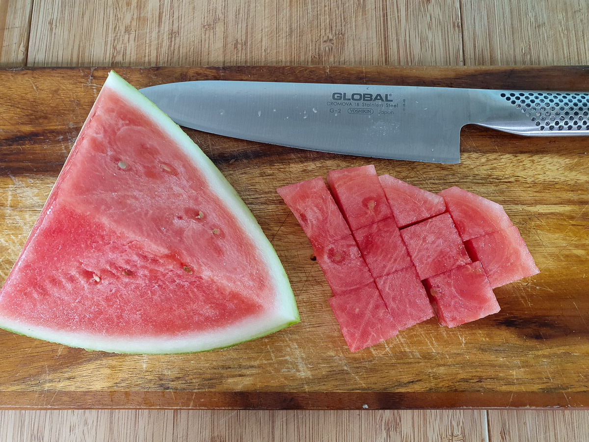 Cutting up watermelon into chunks and cutting off rind.