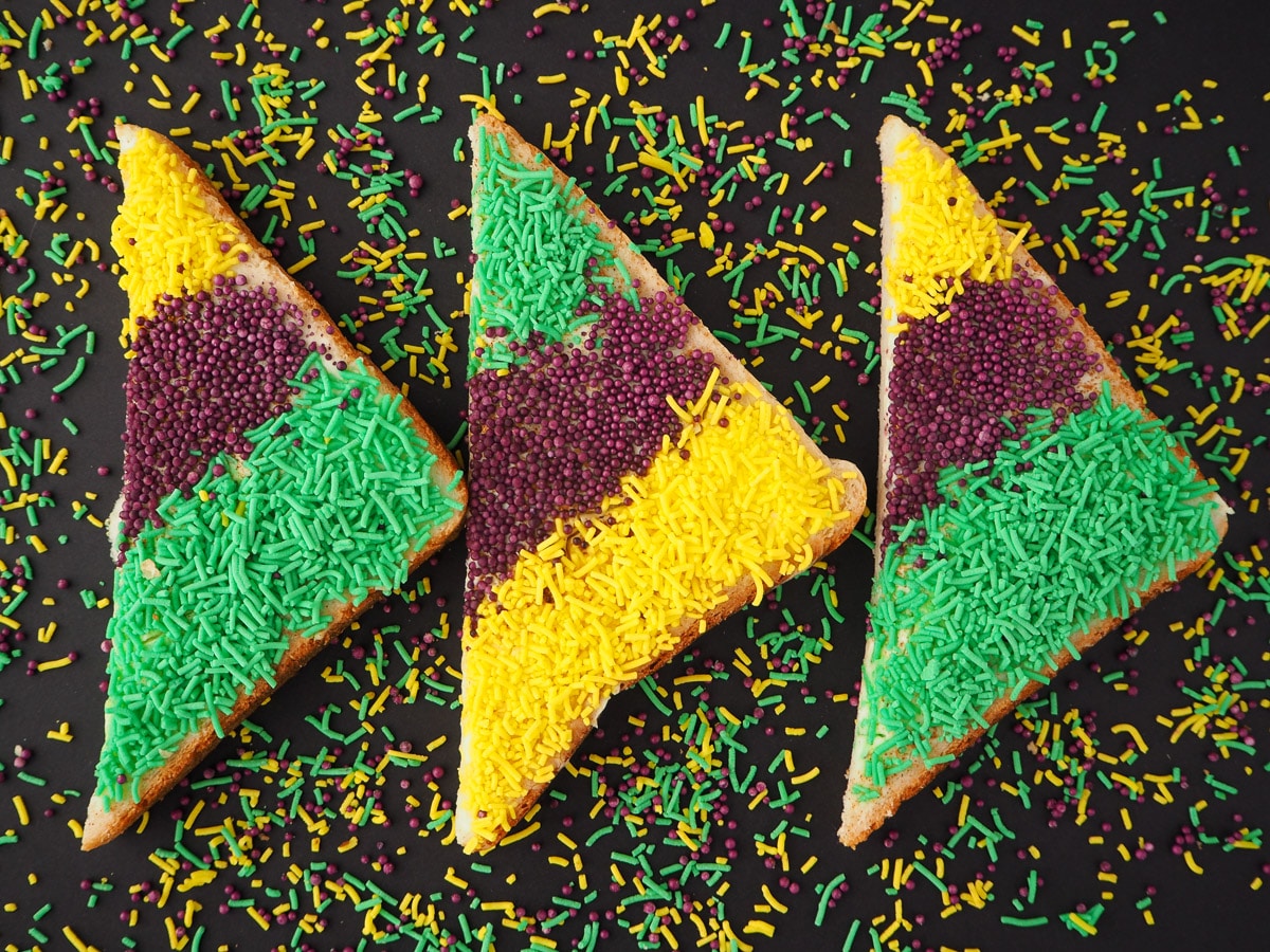 Horizontal line of three slices of King cake sprinkles bread, surrounded by sprinkles.