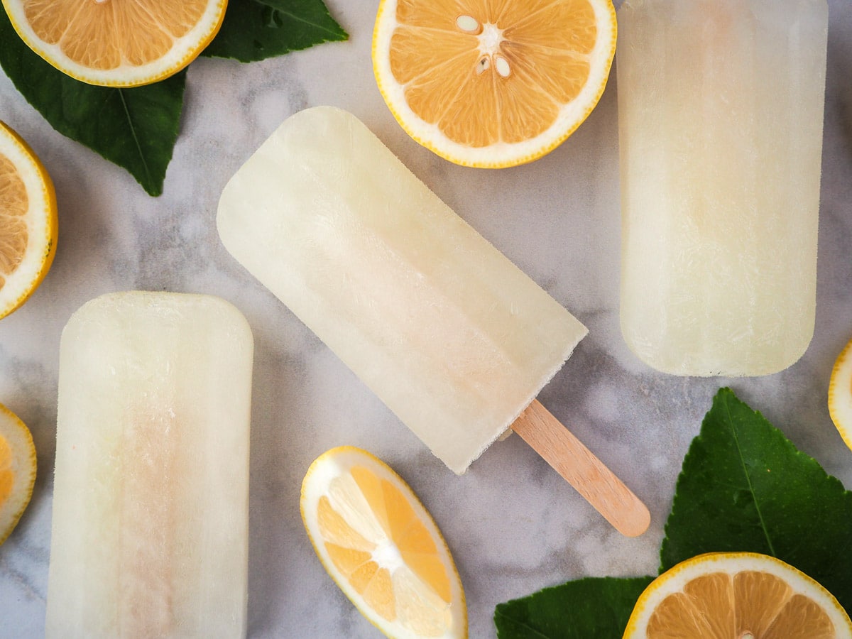 Lemonade popsicles surrounded by fresh lemon slices and lemon leaves.