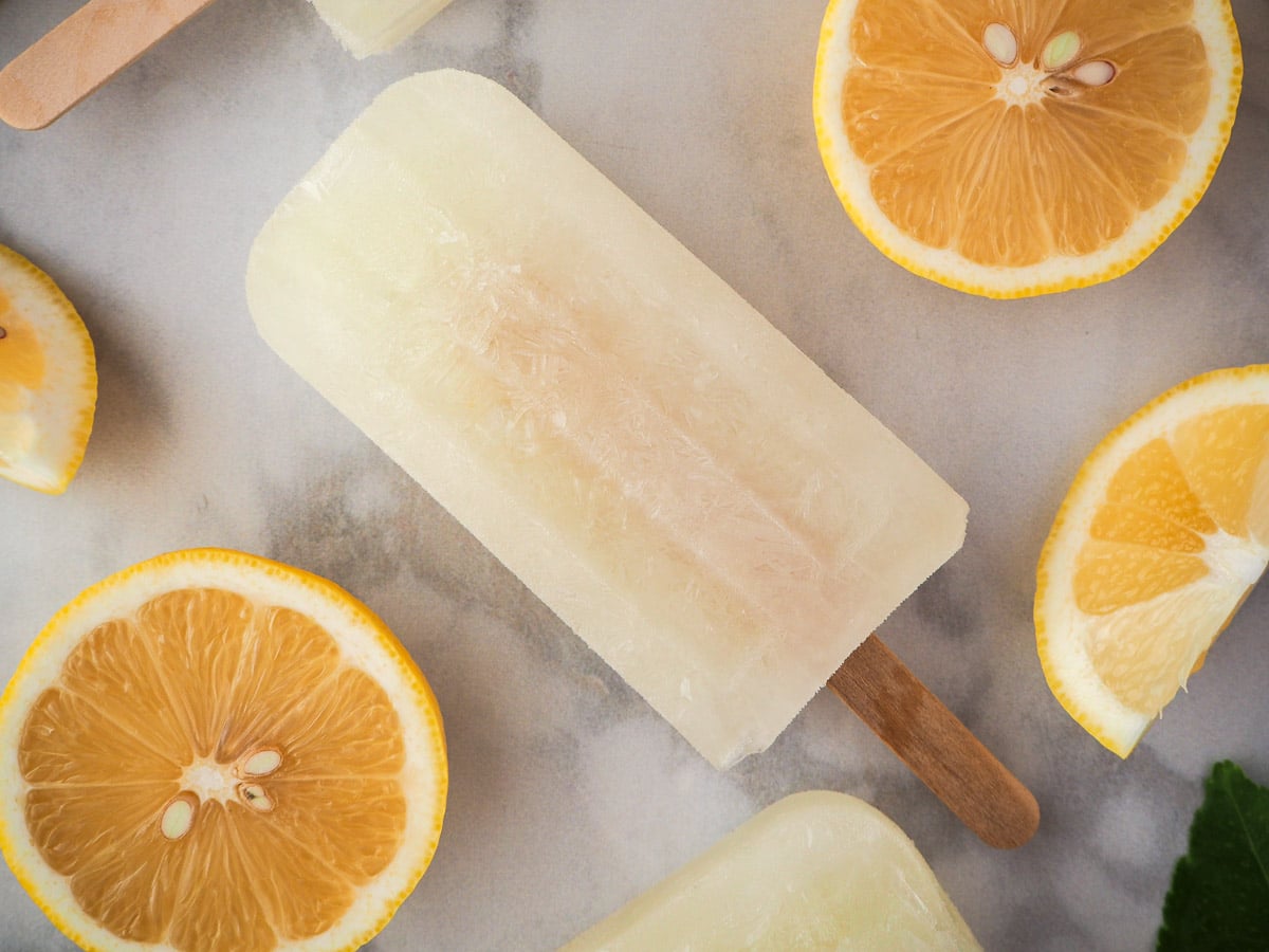 Close up of lemonade popsicles surrounded by fresh lemon slices and lemon leaves..