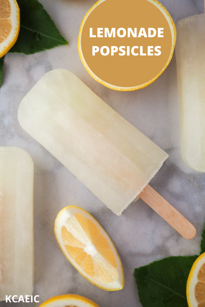 Lemonade popsicles surrounded by fresh lemon slices and lemon leaves, with text overlay, Lemonade popsicles and KCAEIC.