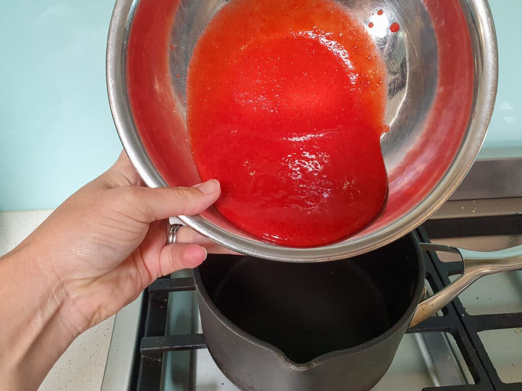 Pouring blitzed strawberries into pot on stove.