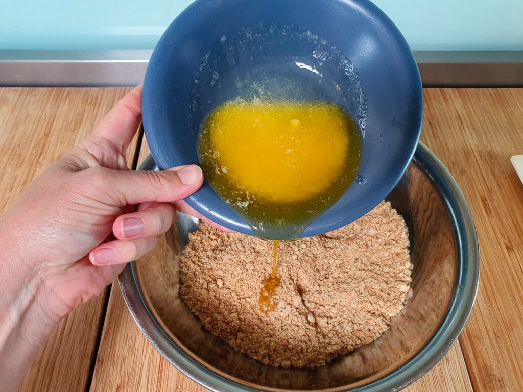 Adding melted butter to biscuit crumbs.