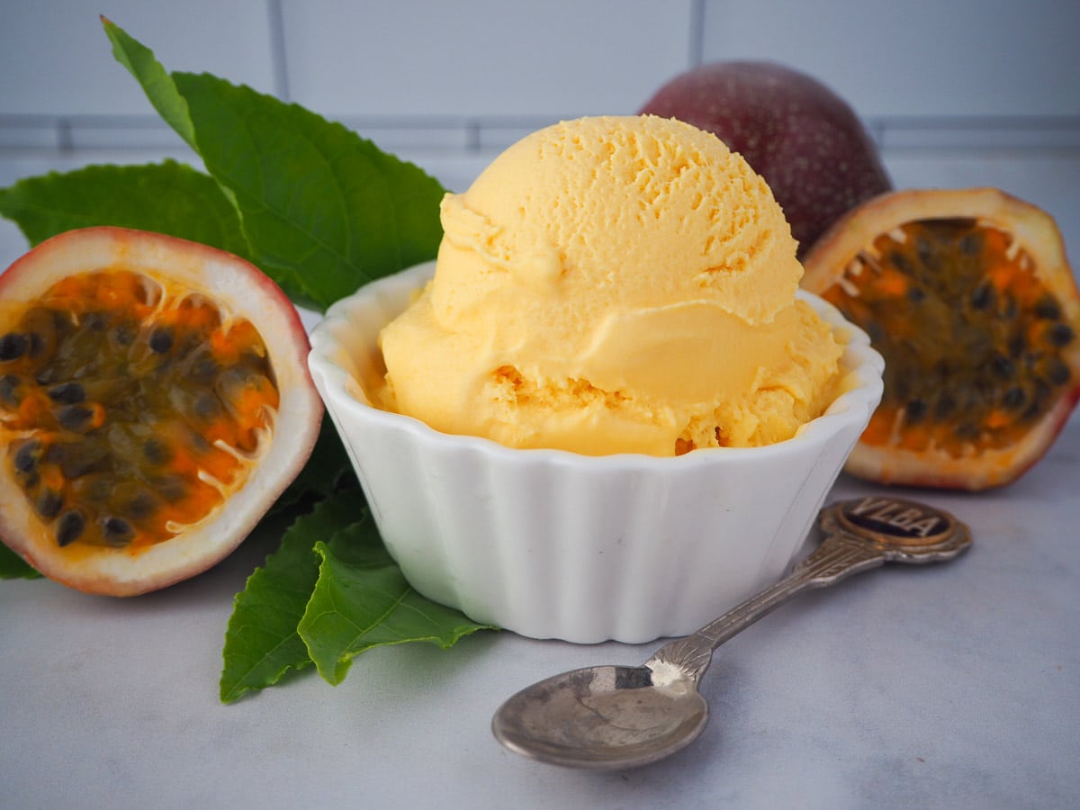 Scoop of passion fruit ice cream with fresh passion fruit and passion fruit leaves and a vintage spoon.