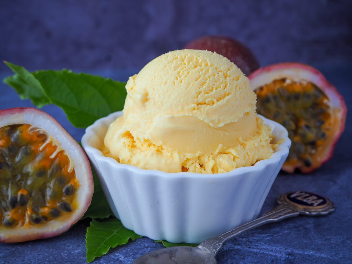 Scoop of passion fruit ice cream with fresh passion fruit and passion fruit leaves and a vintage spoon