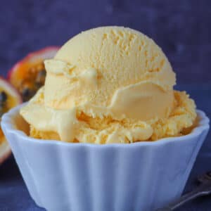 Close up of a scoop of passion fruit ice cream with fresh passion fruit in the background.