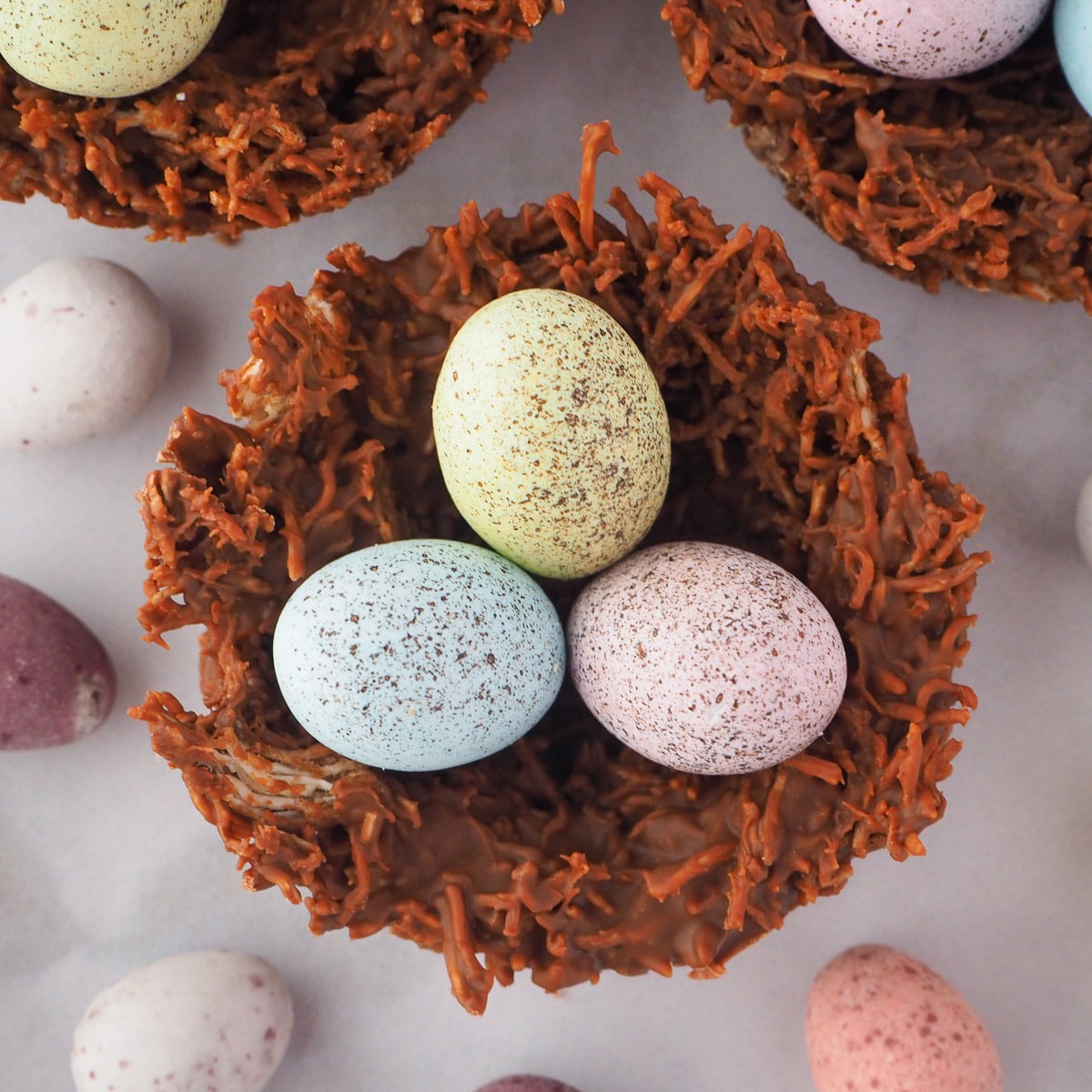 Close up top down view of shredded wheat nests, surrounded by extra speckled Easter eggs.