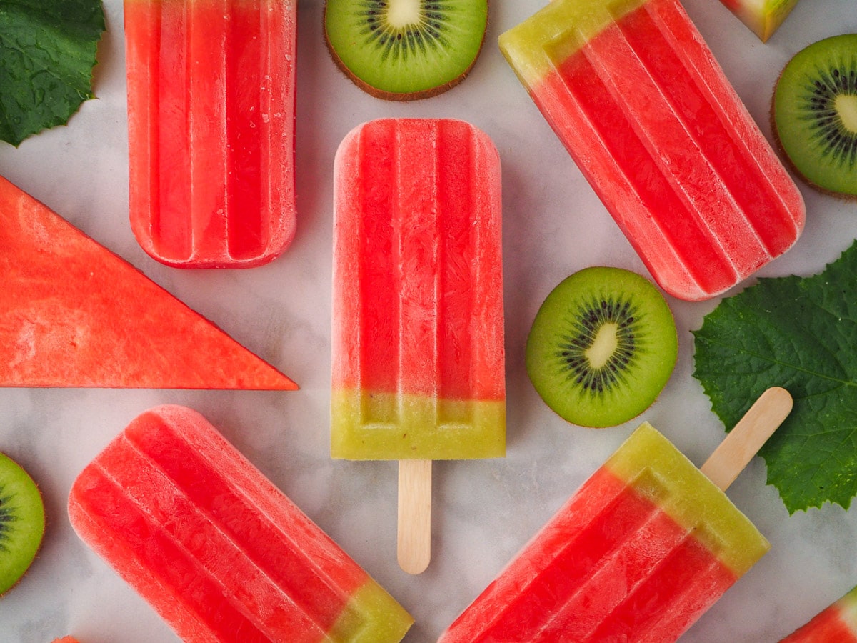 Watermelon ice lollies surrounded by fresh watermelon, watermelon leaves and kiwi fruit.