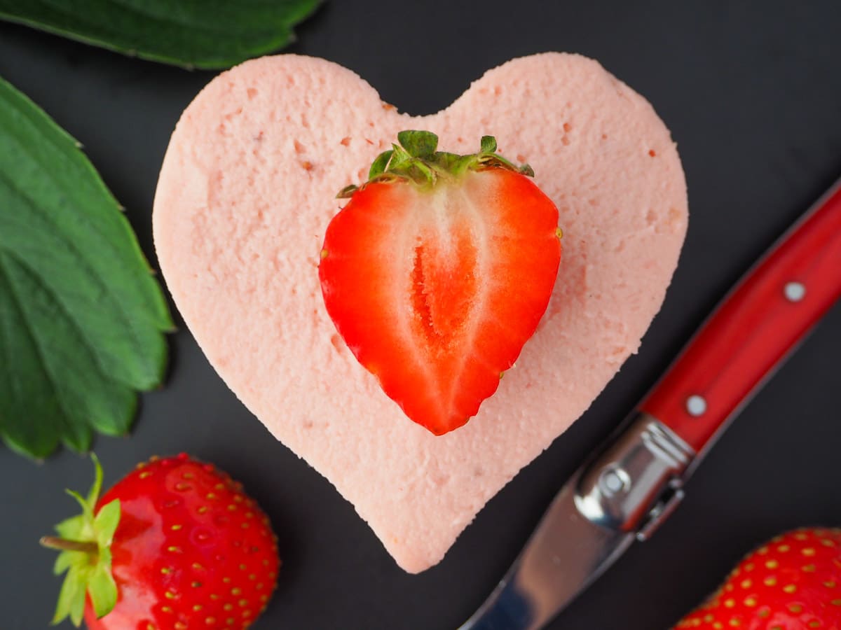 Heart shaped mini strawberry cheesecake with fresh strawberries, fresh strawberry leaves and a vintage fork.