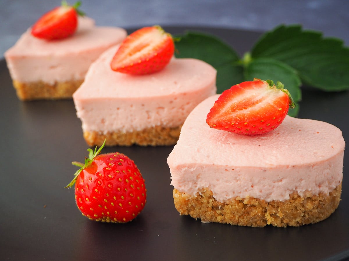 Side view three mini strawberry cheesecakes with fresh strawberries and strawberry leaves.