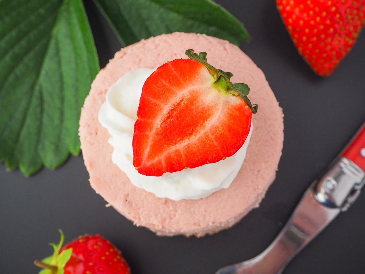 Round mini strawberry cheesecake with whipped cream, fresh strawberries, fresh strawberry leaves and a vintage fork.