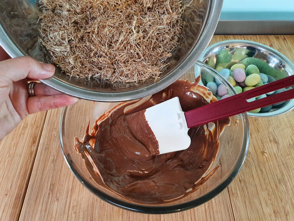 Adding broken up shredded wheat to melted chocolate.