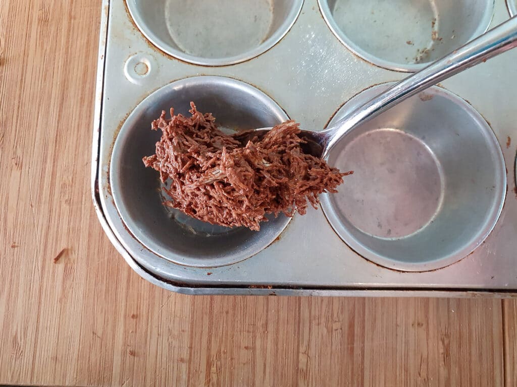 Spooning chocolate and shredded wheat into muffin tins.