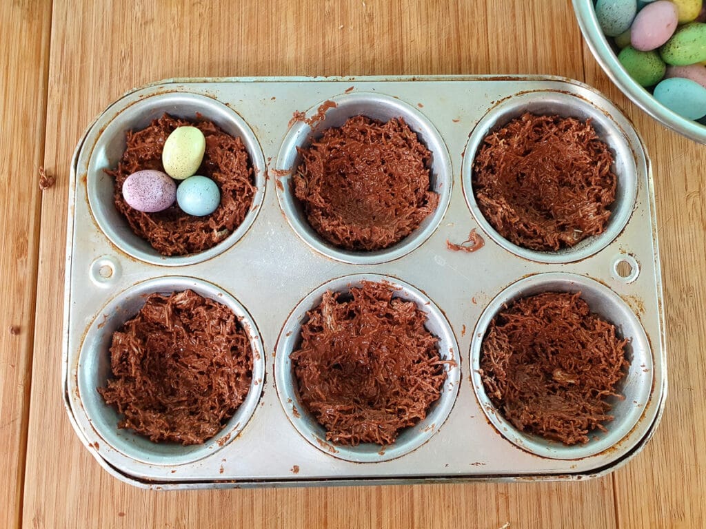 Adding Easter eggs to shaped nests in muffin tins.