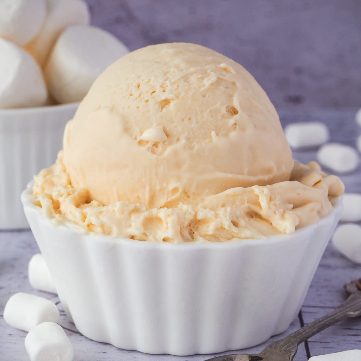 Close up scoop of marshmallow ice cream in a decorative white bowl, with vintage spoon on the side and bowl of marshmallows in the background.