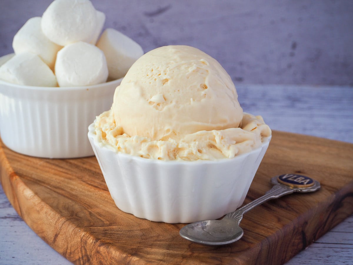 Scoop of marshmallow ice cream in a decorative white bowl, with vintage spoon on the side and bowl of marshmallows in the background.