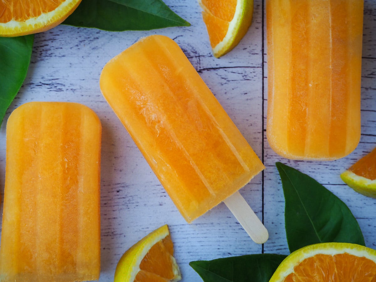 Orange popsicles with fresh oranges and orange leaves.