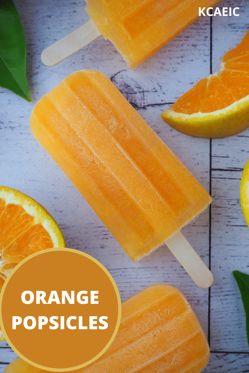 Orange popsicles in a vertical row, with fresh orange and orange leaves and text overlay, orange popsicles, KCAEIC.