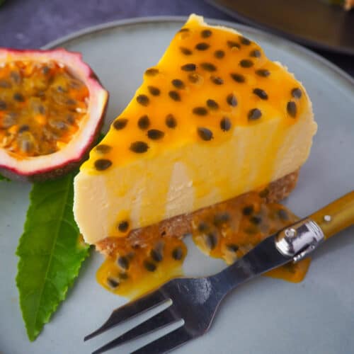 Close up passion fruit cheesecake with passion fruit coulis, a vintage fork in front, fresh passion fruit and passion fruit leave on the side.