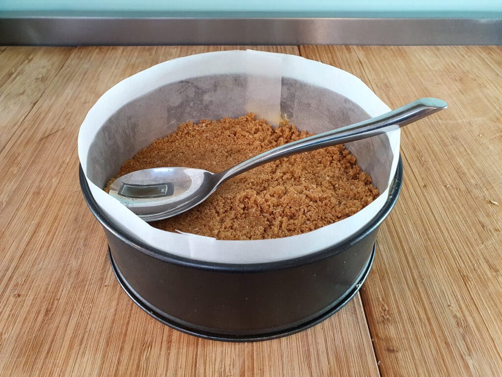 Pressing down cheesecake base into tin with back of large spoon.