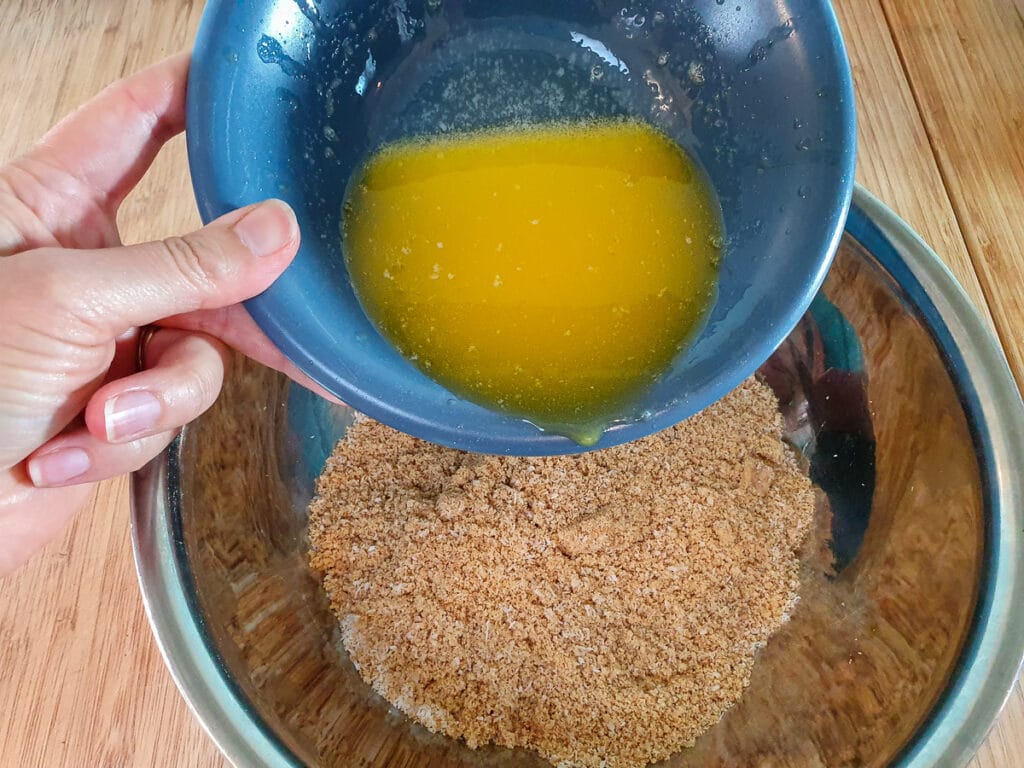 Adding melted butter to biscuit crumbs and coconut.